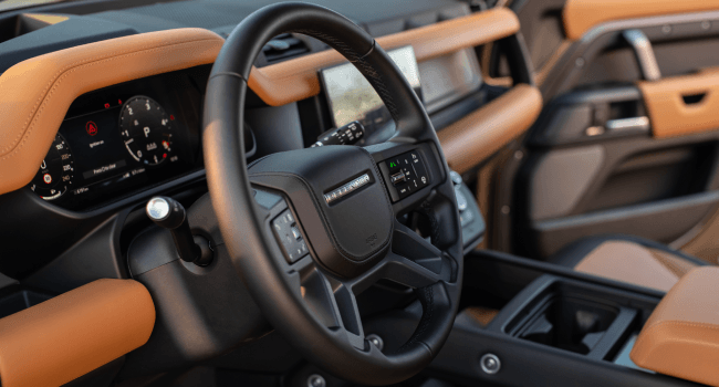 Land Rover Defender interior, featuring a premium steering wheel, digital display, and eye-catching orange leather.